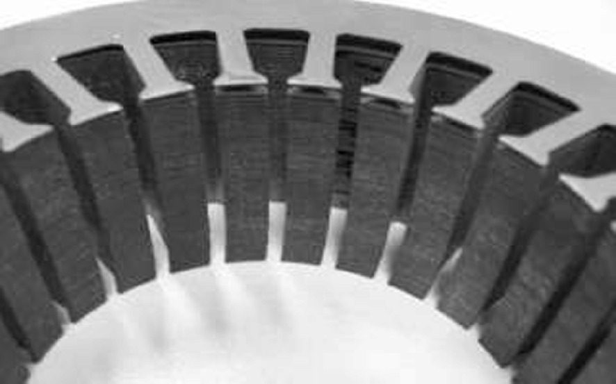 A close-up photo of a circular metallic structure with evenly spaced vertical slots or teeth, resembling a component of a mechanical or electrical device. The image highlights the texture and arrangement of the slots, suggesting functionality related to machinery or engineering. The background is plain, emphasizing the structure's design.