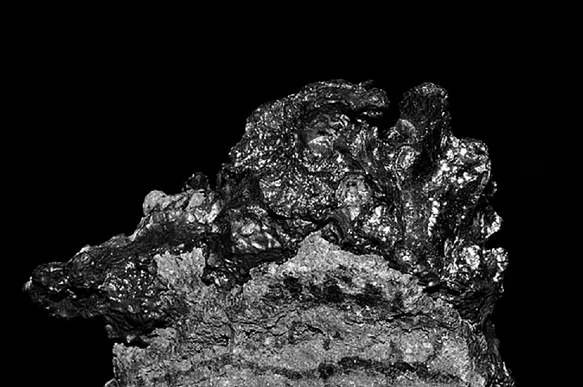 An electron microscopy image showing a highly detailed, textured surface of a material. The image highlights the intricate, rough, and uneven structure, with various peaks and valleys, against a dark background. The surface appears metallic and crystalline, showcasing the complexity and fine details visible at a microscopic level.