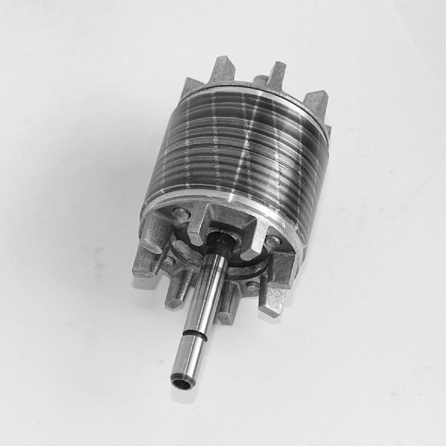 A metallic cylindrical component with a central shaft extending outward, featuring multiple stacked layers and protruding fins around its circumference. The object is placed on a plain surface, and the image is in grayscale.